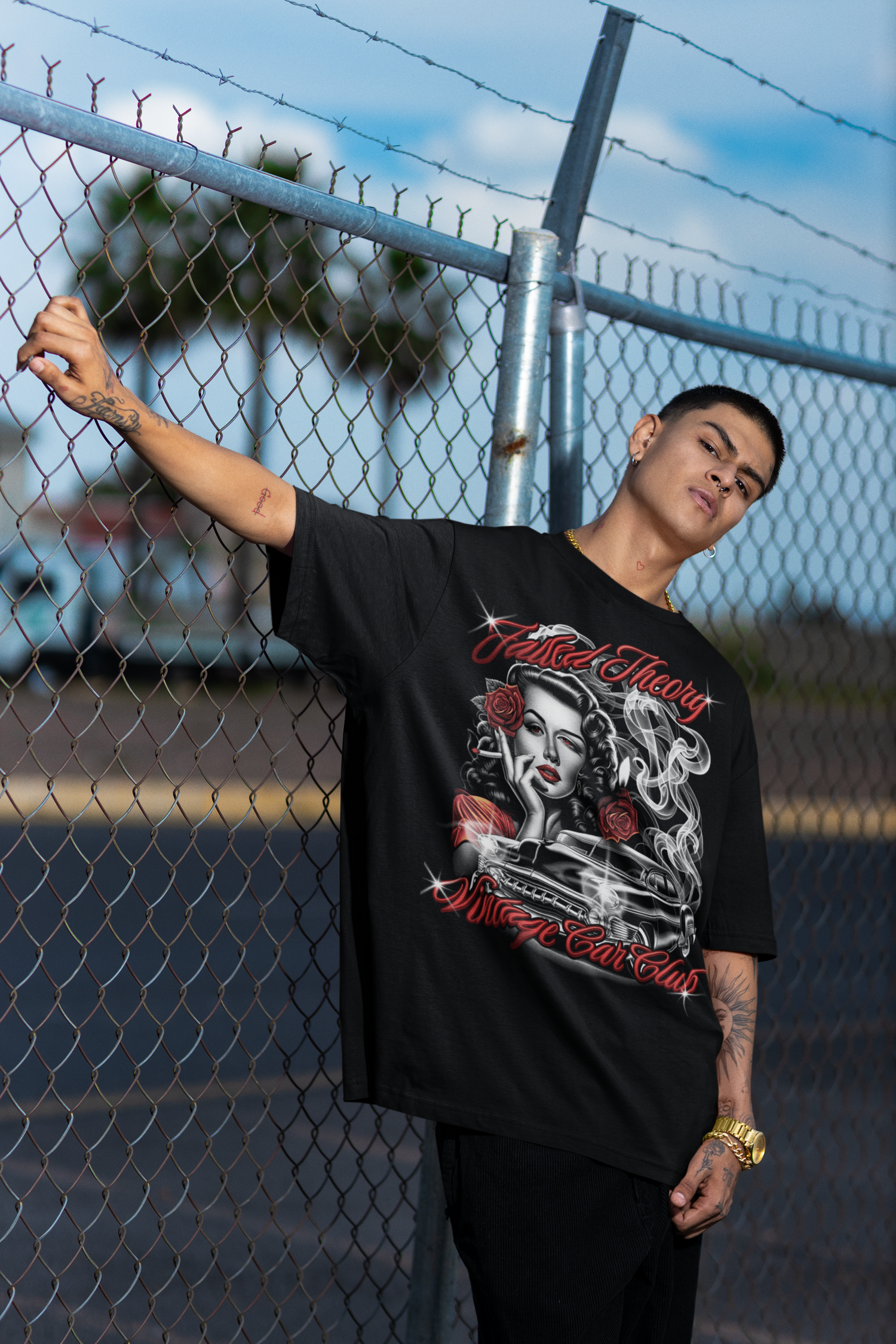 Person wearing a black t-shirt with graphic design leaning against a chain-link fence.